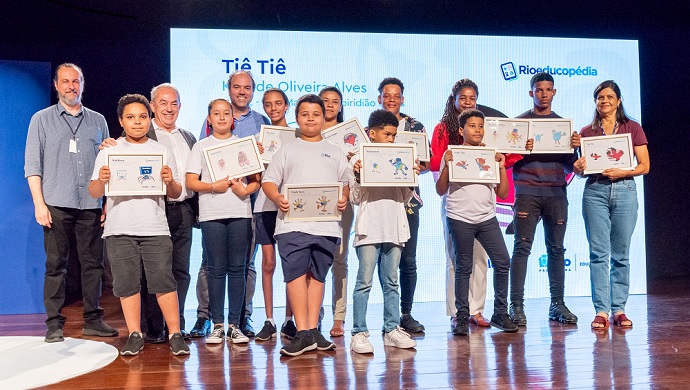 Crianças e adolescentes posam, em cima de um palco, com seus certificados de vencedores do concurso